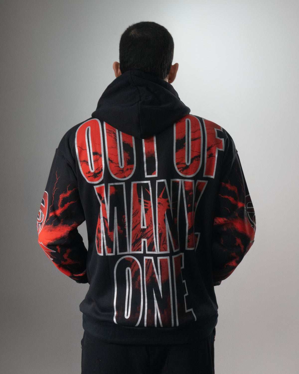 Espalda del buzo negro del conjunto Liberty con la frase OUT OF MANY, ONE en letras rojas